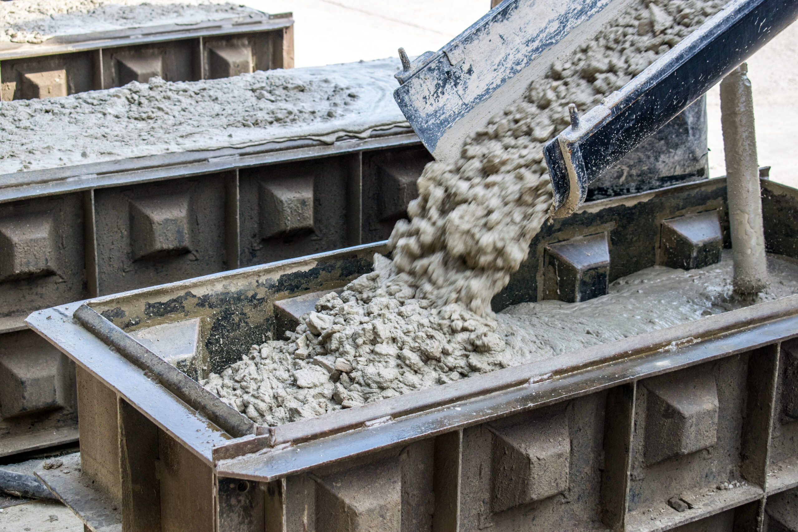 Herstellung von Betonbausteinen: Frischbeton wird in verzahnte Schalungsformen gegossen